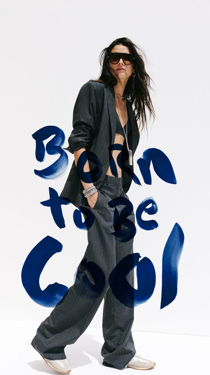 A model wearing a striped outfit with sunglasses, a necklace, and sneakers. Featuring the &ldquo;Born to be cool&rdquo; logo