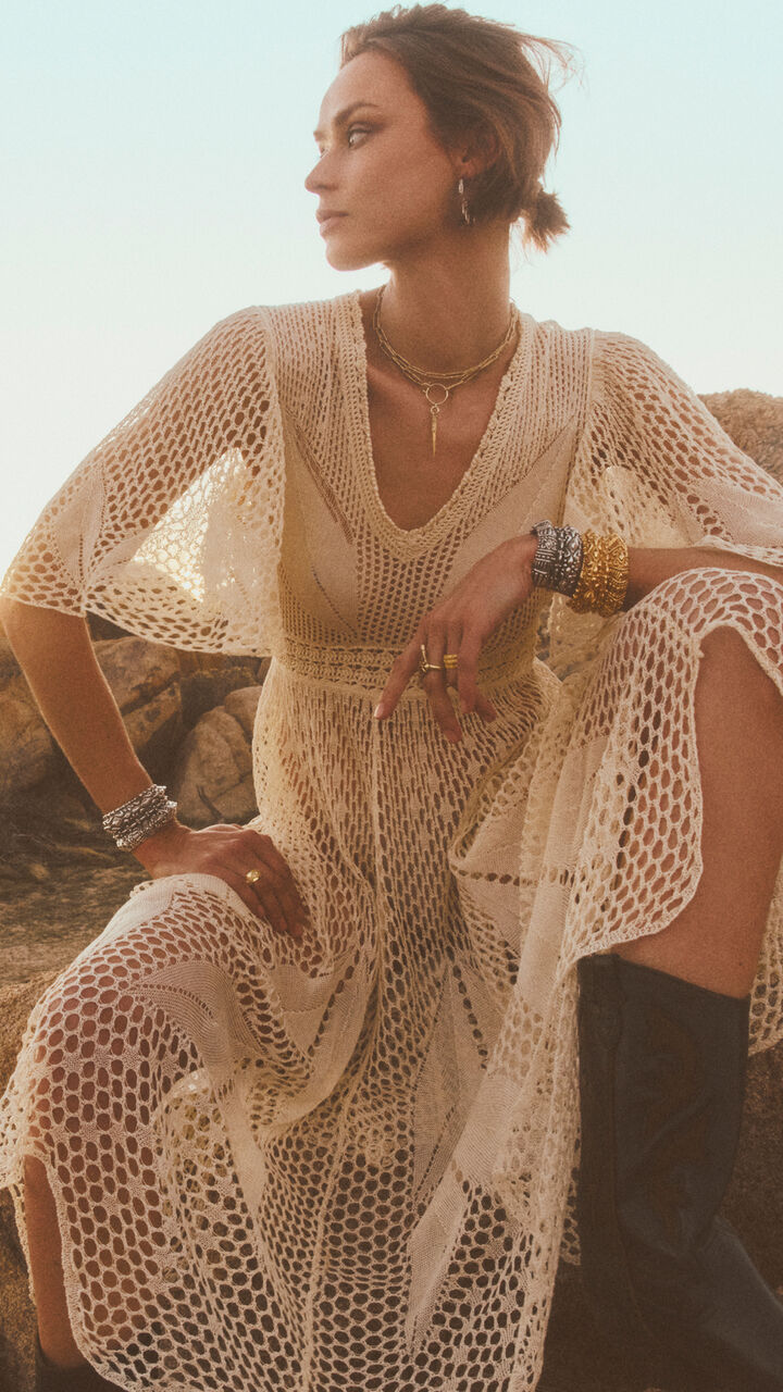 A model wearing a whitedress and several necklaces and bracelets