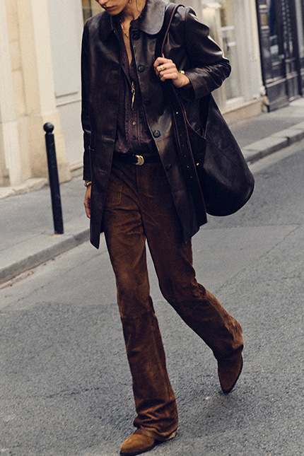 The model is wearing a leather coat, suede pants and ankle boots