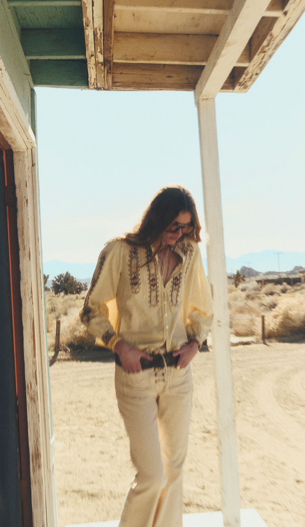 a model wearing a loose-fitting blouse and light-colored pants with a wide belt in the desert