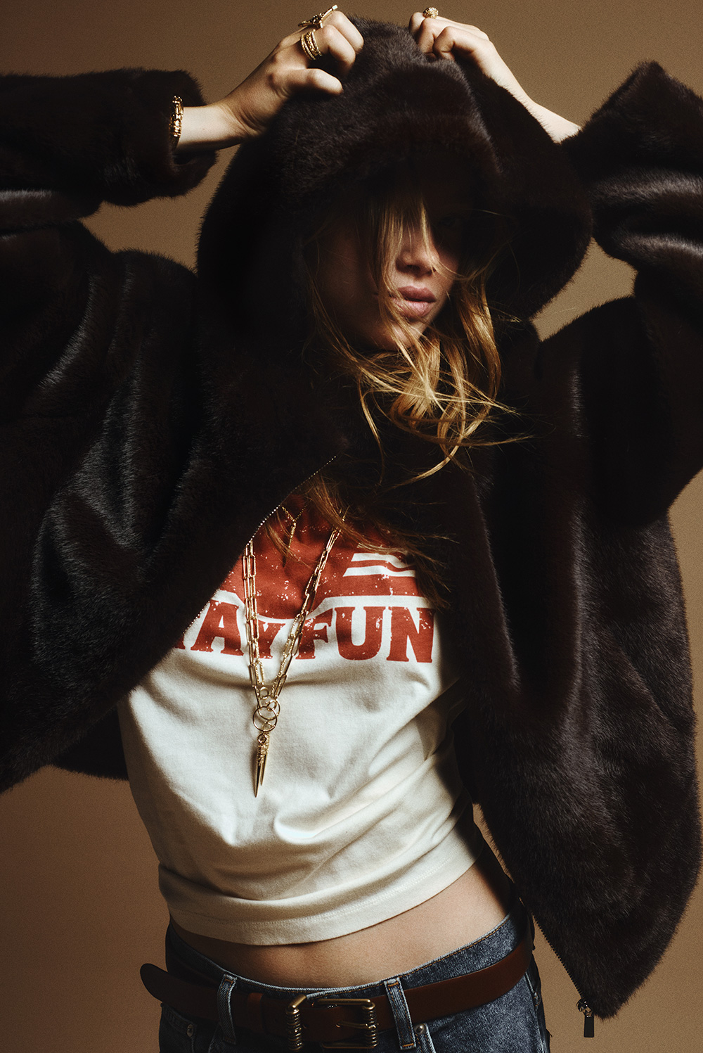 Model wearing a black fur hooded jacket, gold necklaces and a white logo t-shirt
