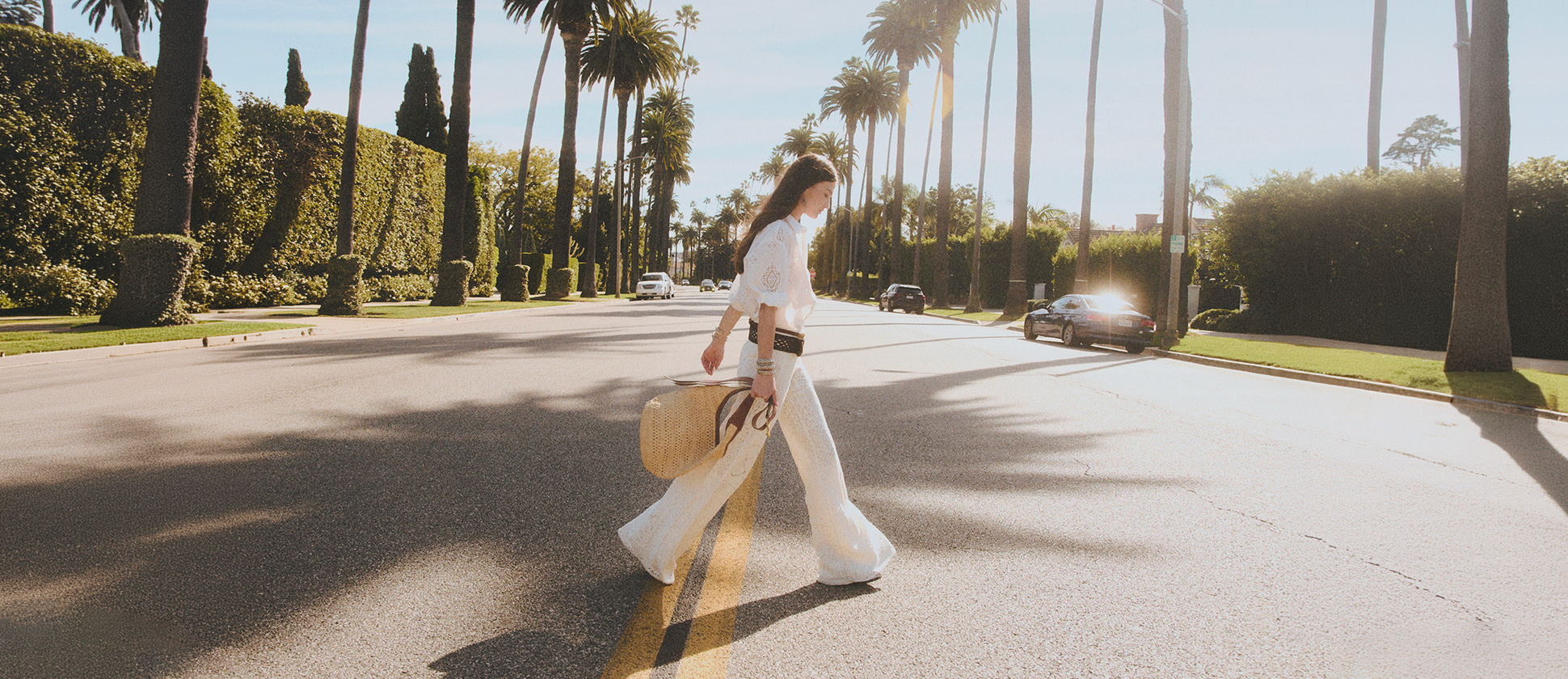 A model wearing white pant, white skirt and raffia youyou and  walking in the street