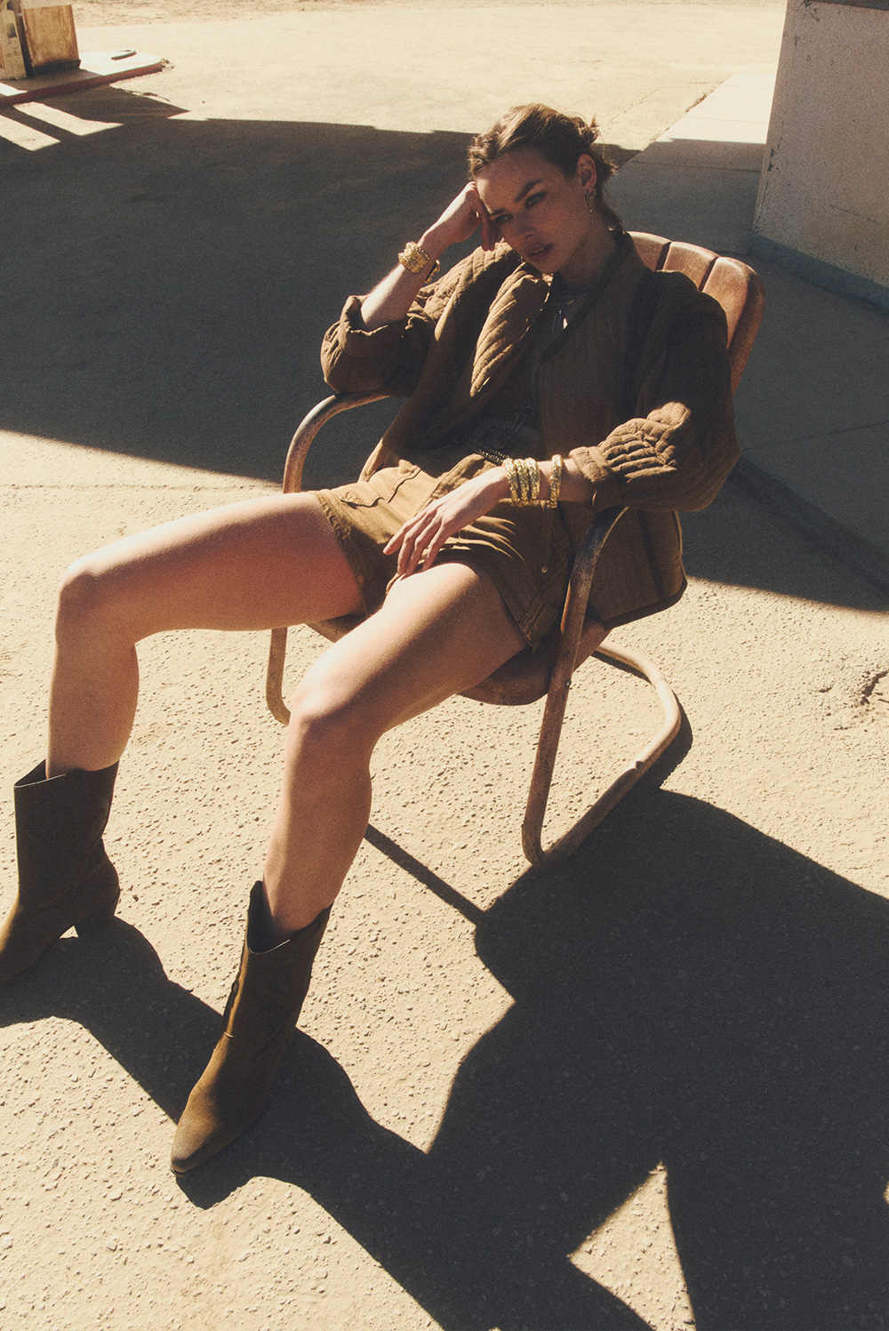a model wearing a khaki jacket and khaki shorts on a chair 