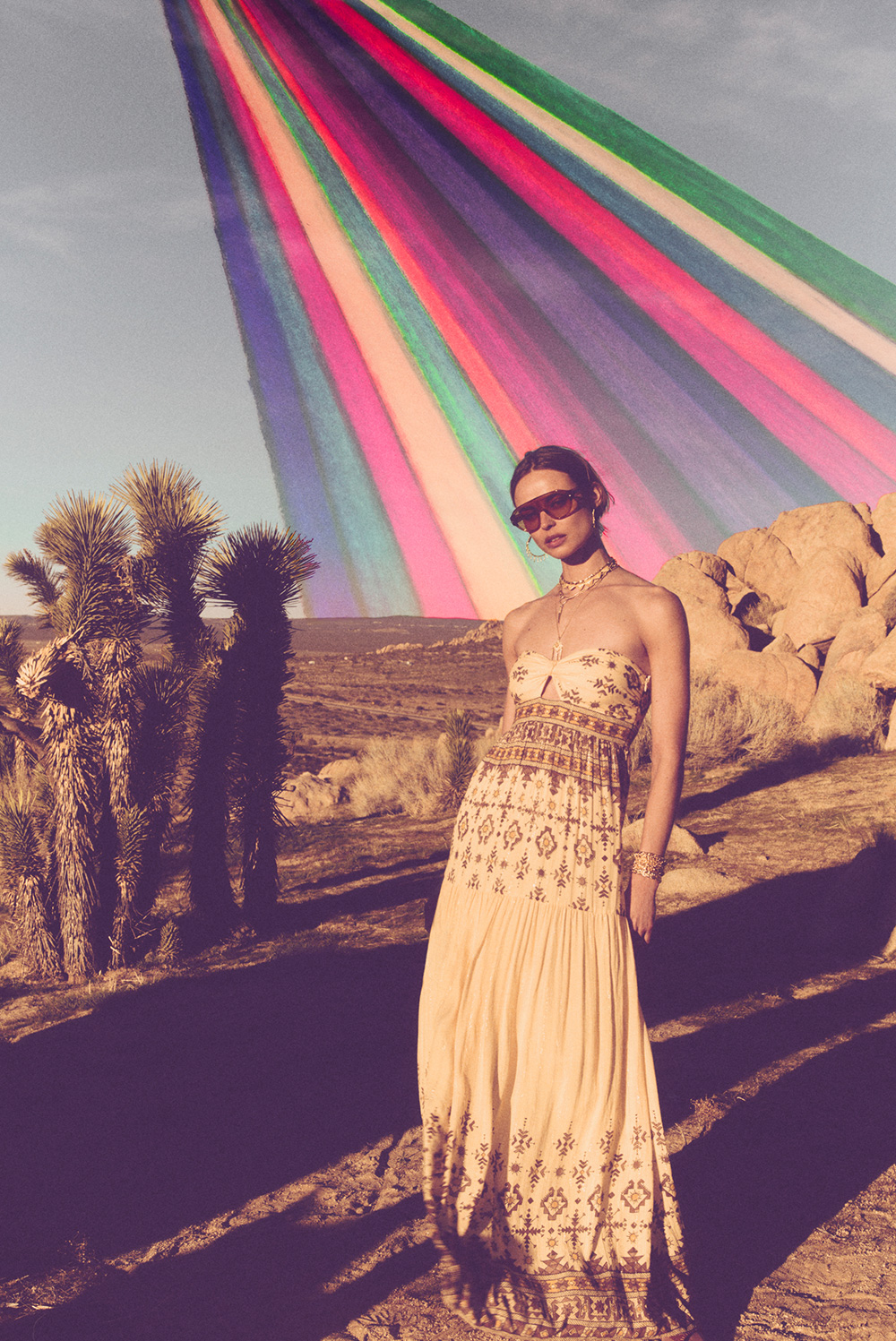 a woman in a yellow printed dress standing in front of a rainbow