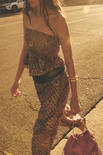 a model walking down the street wearing a patterned top and pant, a belt, and a bag
