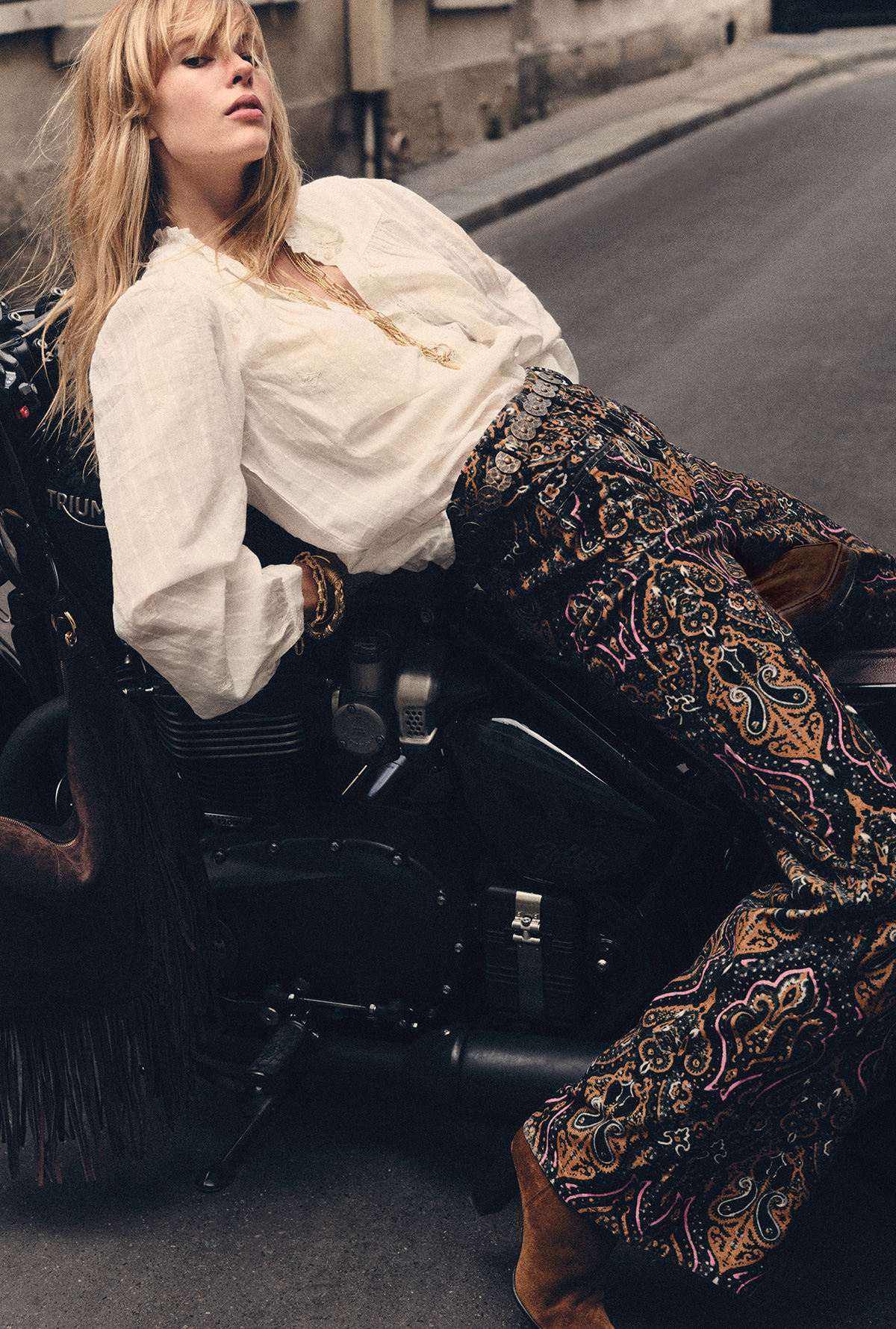 blond hair model on a bike, wearing printed pants and a white long wide sleeves blouse