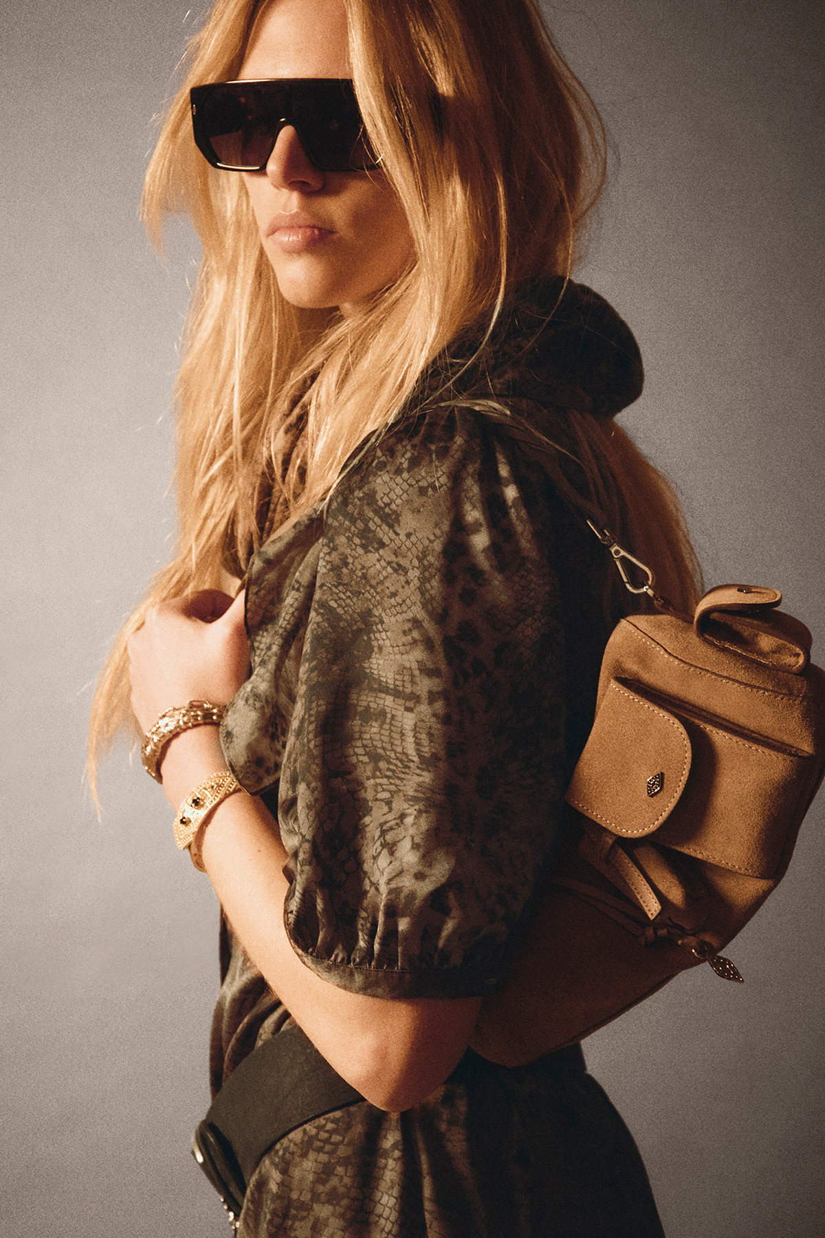 a model wearing a khaki snake print blouse with a brown multipocket handbag and sunglasses