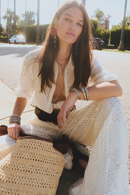 a model sitting on the street wearing a white dress and raffia bag