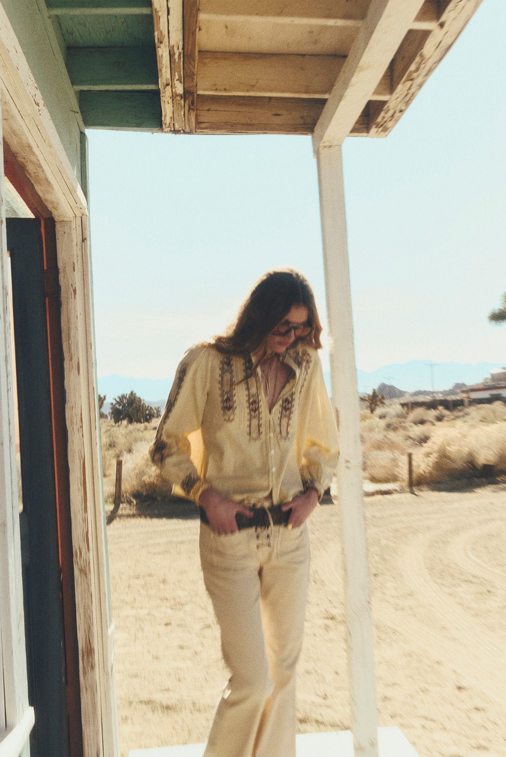 a model wearing a loose-fitting blouse and light-colored pants with a wide belt in the desert
