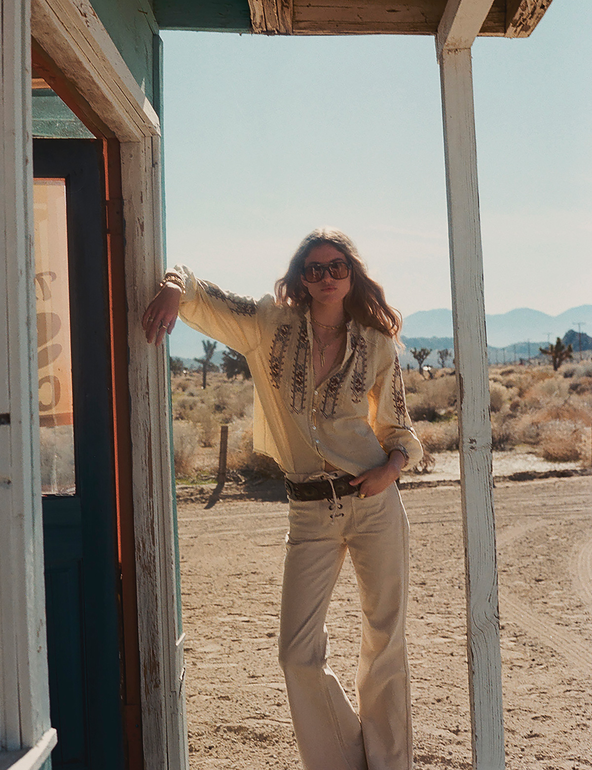 A blonde model wearing a blouse and light-colored pants with a thick belt in a California desert.