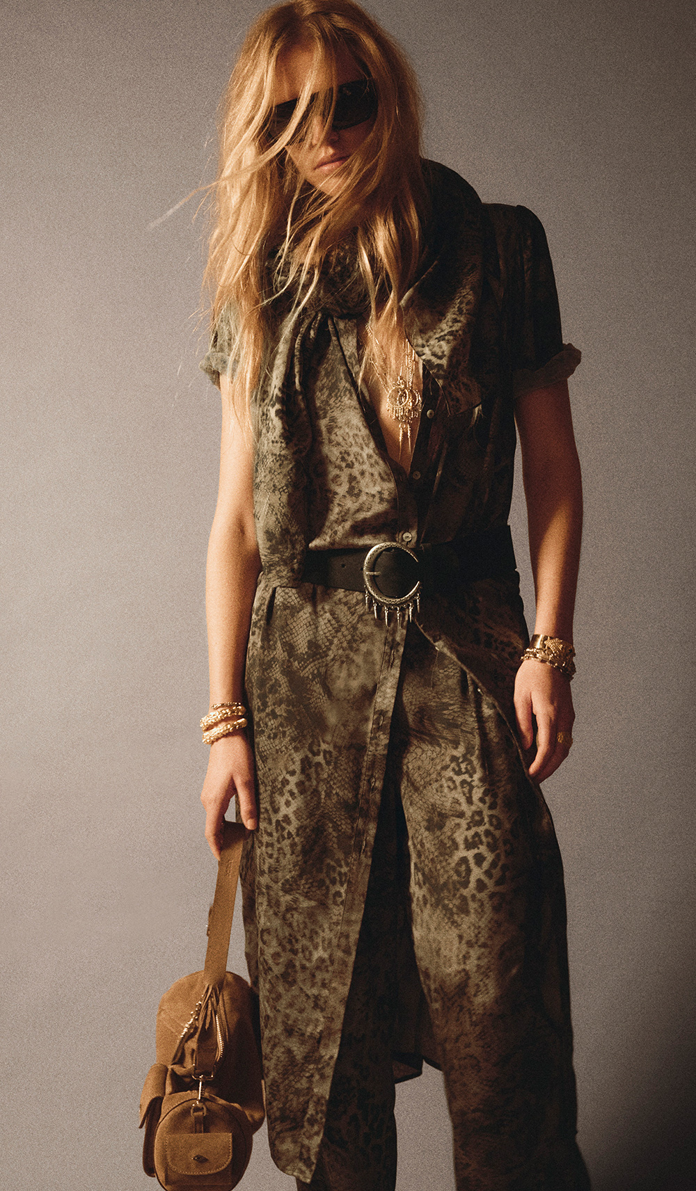 Model wearing a green snake printed dress, with the matching print trousers and a brown suede bag