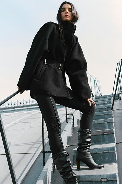 The model is wearing a long striped coat, a knit sweater, jeans, and suede ankle boots 