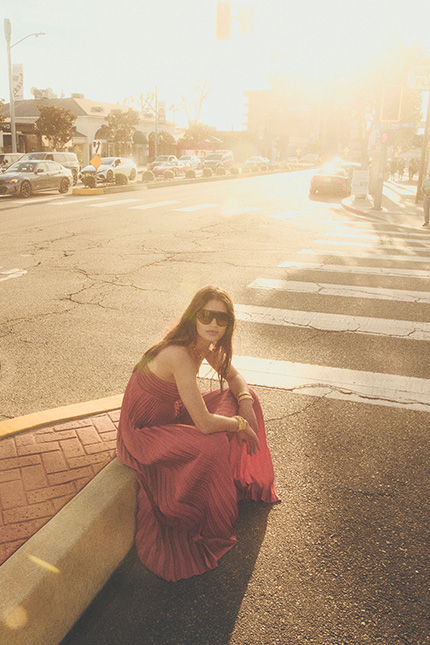 a model sitting on the street wearing a pink dress