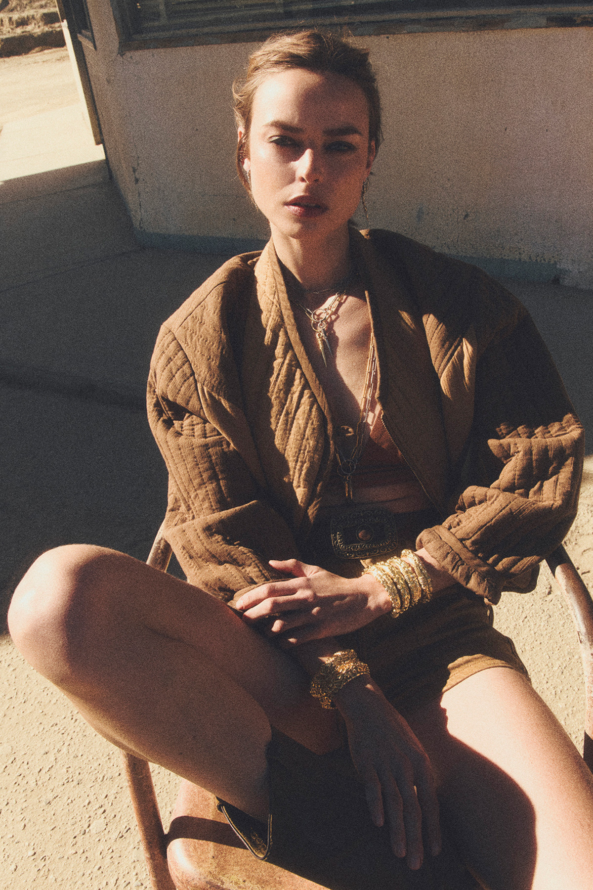 a blonde model wearing a camel-colored quilted jacket, sitting on a chair