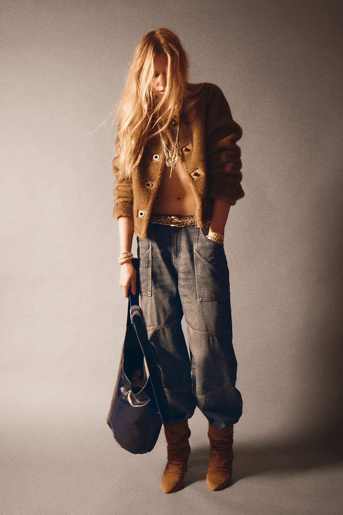 A model wearing a brown jacket with the ba&sh YouYou bag, a pair of jeans and brown suede boots