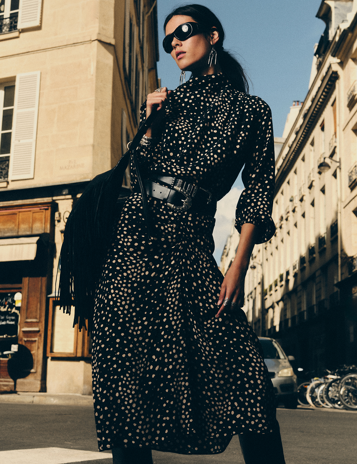 Brunet woman wearing black dress and sunglasses, and holding a black bag.