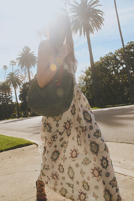 a model walking down the street wearing a patterned dress and a bag