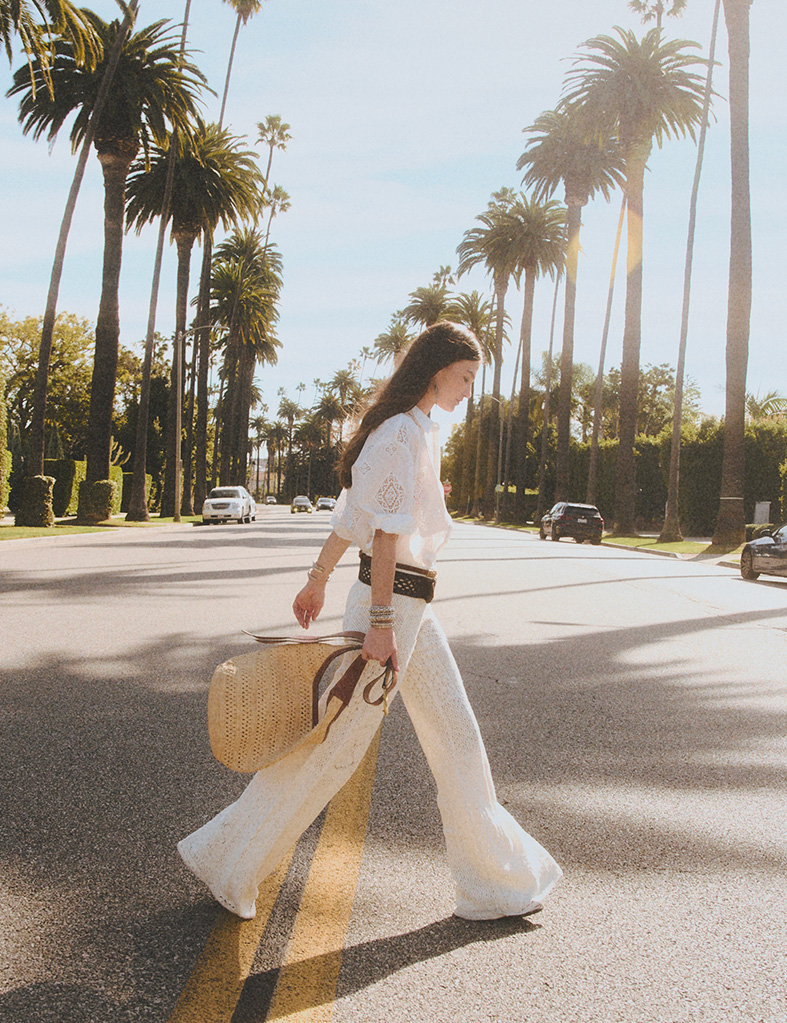 A model wearing white pant, white skirt and raffia youyou and  walking in the street