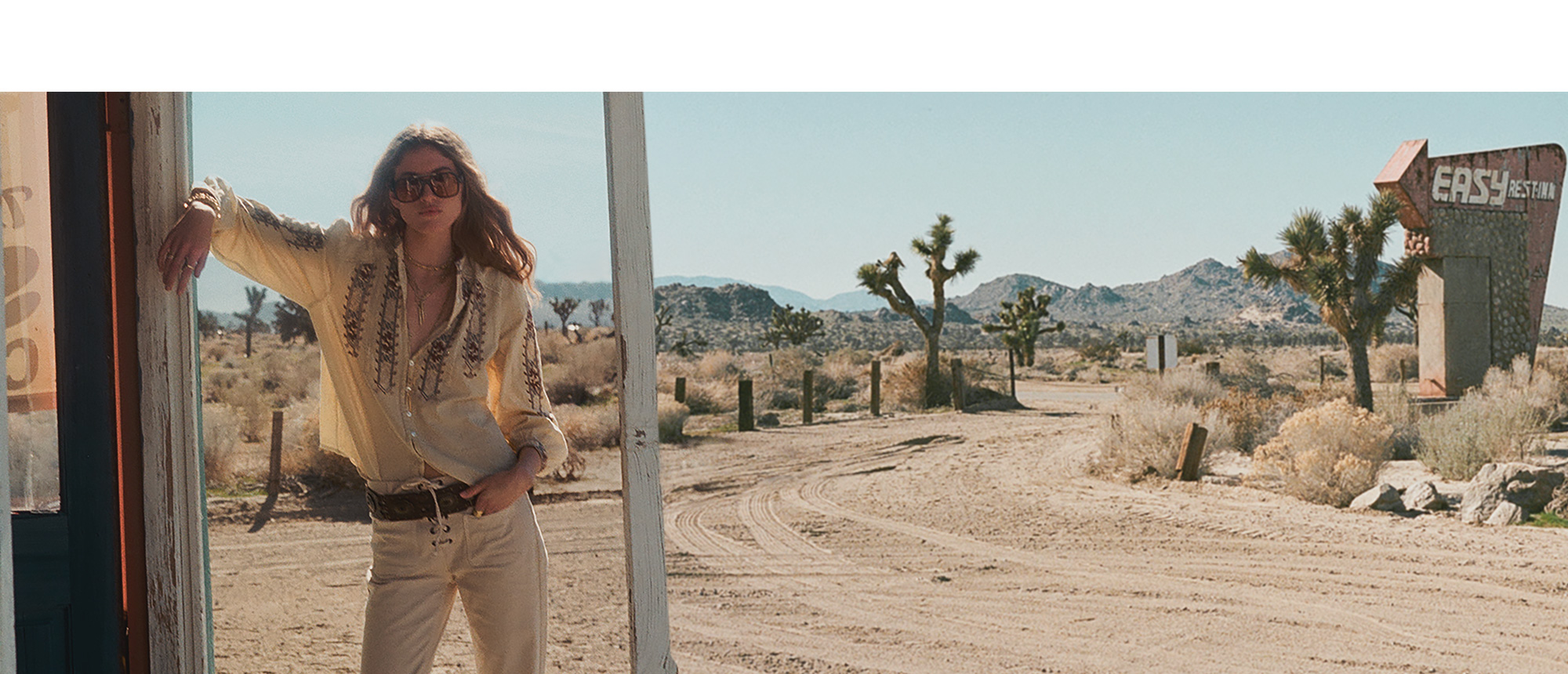 A blonde model wearing a blouse and light-colored pants with a thick belt in a California desert.