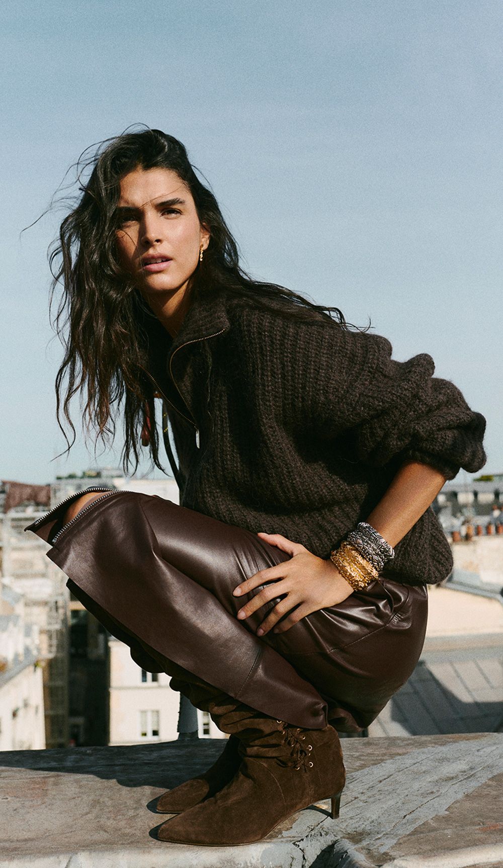 The model is wearing a knit sweater, a leather skirt, and boots